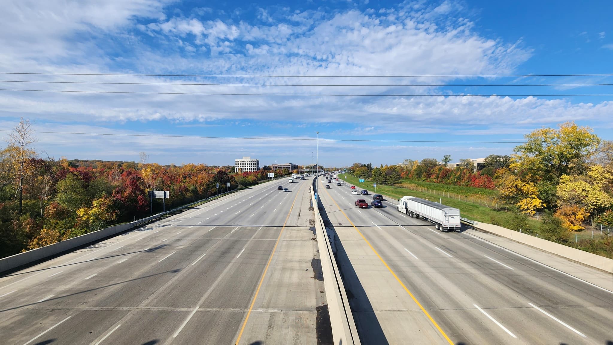 A wide highway with autumn trees on the sides under a blue sky with scattered clouds