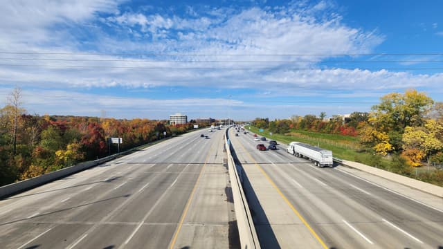 A wide highway with autumn trees on the sides under a blue sky with scattered clouds