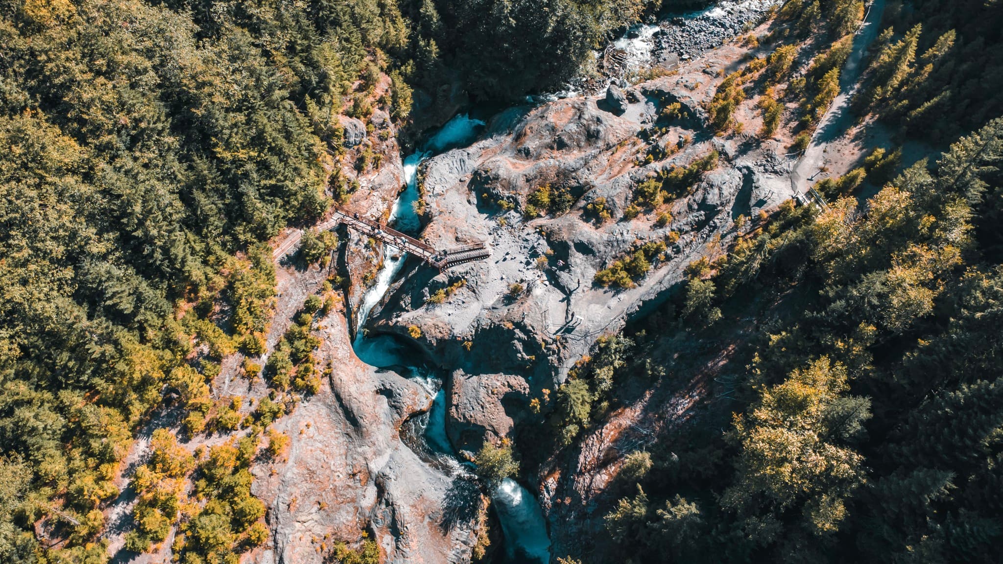 Aerial view of a turquoise river winding through a rocky canyon surrounded by forested hills