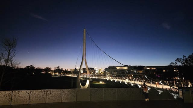 Illuminated cable-stayed bridge with a distinct A-frame pylon against a dark blue twilight sky