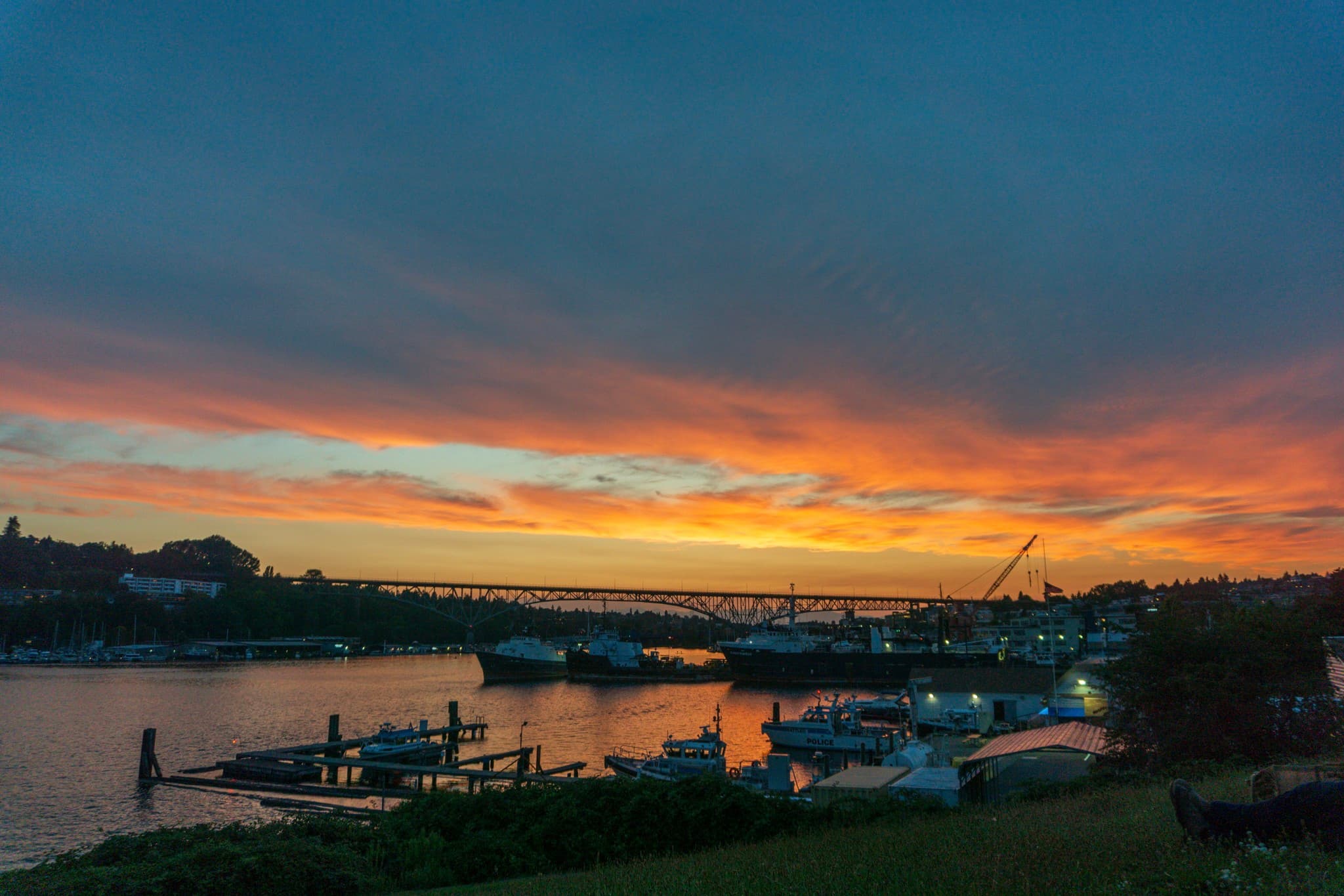 A vertical collage of four images depicting a harbor scene with boats docked near the shore under a colorful sunset sky