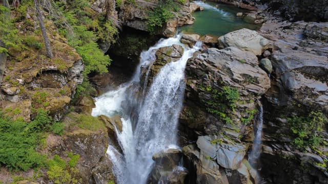 A vertical shot captures a waterfall tumbling down a rocky cliff face, surrounded by green vegetation and leading into a calm pool of water.
