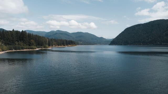 A wide lake surrounded by tree-covered hills and mountains under a cloudy sky